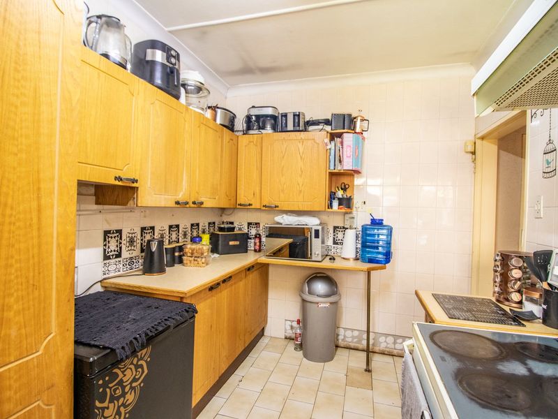 A dated kitchen featuring wood-look laminate cabinetry, tiled splashbacks, and ceramic flooring, equipped with a built-in electric hob and extractor fan.