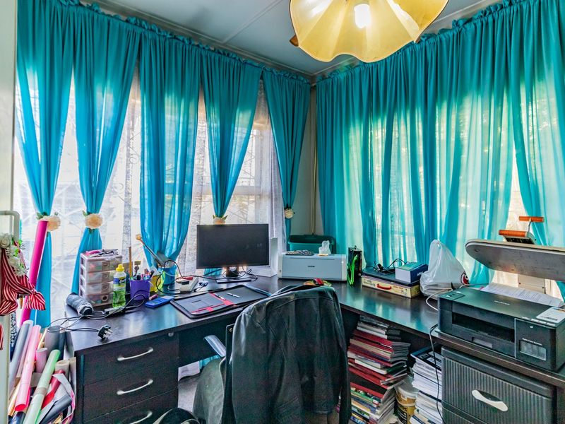 A functional home office space featuring large windows with bright curtains and ample desk space for a productive work environment.
