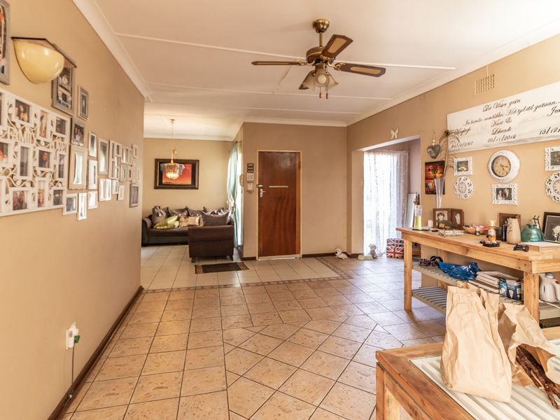A spacious living area featuring tiled flooring, a ceiling fan, and coved ceilings, providing a neutral base for potential interior updates.