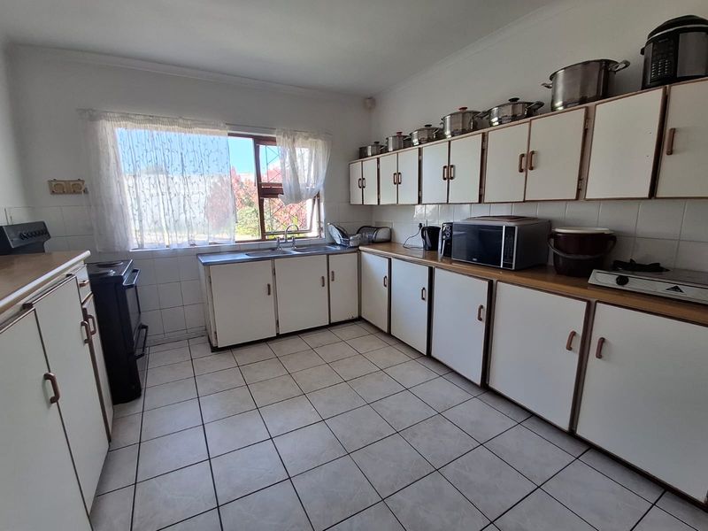 A functional kitchen featuring white built-in cabinetry, laminate countertops, tiled flooring, and a double basin sink with a window view.