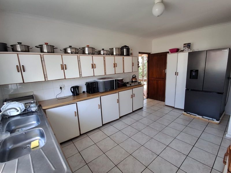 A functional kitchen featuring white cabinetry, laminate countertops, a double stainless steel sink, and tiled flooring with direct access to an outdoor area.