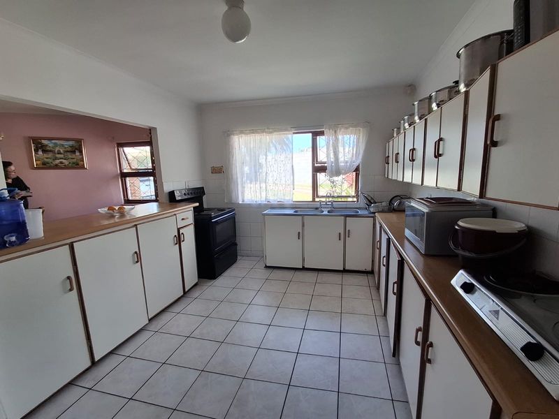 A functional kitchen featuring white cabinetry, laminate countertops, tiled flooring, and a freestanding stove, offering a practical layout with potential for modernization.