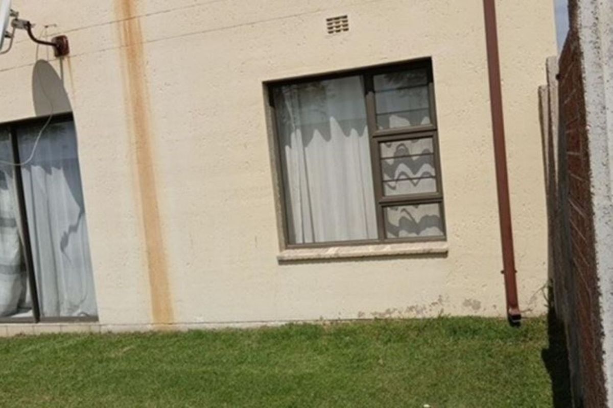 Rear exterior view of the apartment showing a small lawn area, sliding door access, and visible maintenance issues on the exterior wall.