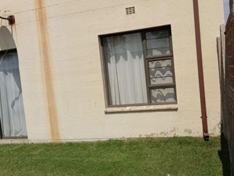 Rear exterior view of the apartment showing a small lawn area, sliding door access, and visible maintenance issues on the exterior wall.