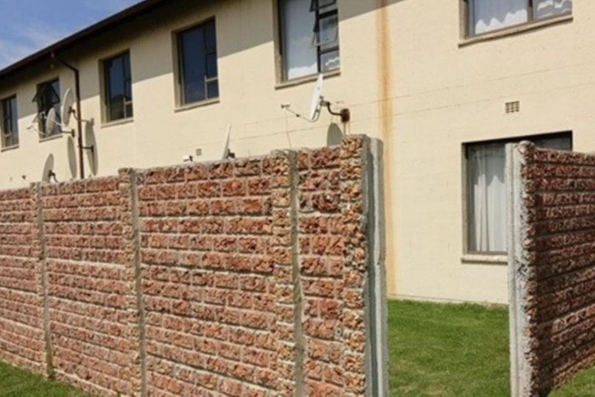 Rear view of the apartment building featuring a brick boundary wall, small lawn area, and exterior wall staining.