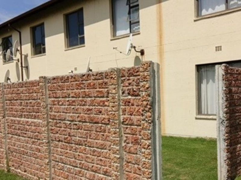 Rear view of the apartment building featuring a brick boundary wall, small lawn area, and exterior wall staining.