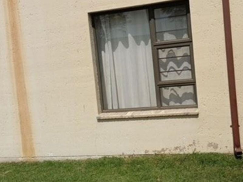 Rear exterior view of the apartment showing a small lawn area, sliding door access, and visible wear on the exterior wall finish.