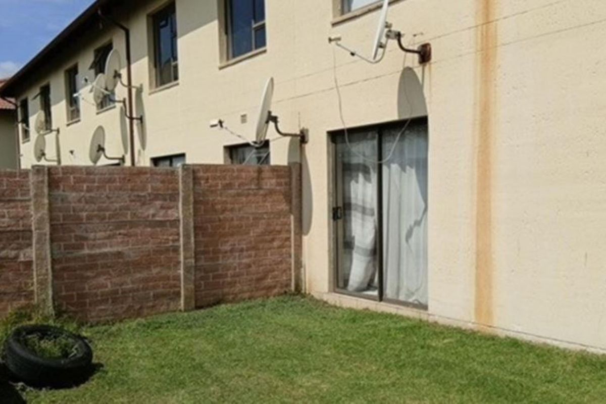 Rear view of the apartment showing a small private garden, brick boundary wall, and sliding door access with visible exterior wall staining.