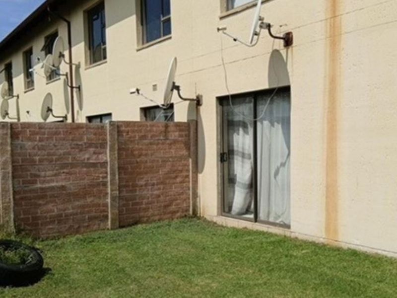 Rear view of the apartment showing a small private garden, brick boundary wall, and sliding door access with visible exterior wall staining.