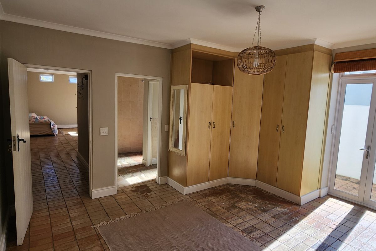 Spacious bedroom featuring built-in wooden cupboards, tiled flooring, and direct access to an outdoor area through glass french doors.
