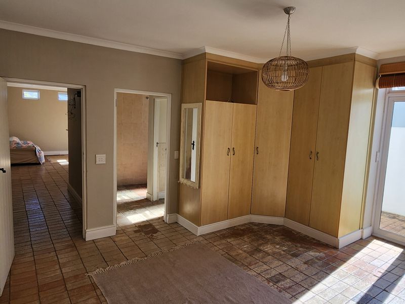 Spacious bedroom featuring built-in wooden cupboards, tiled flooring, and direct access to an outdoor area through glass french doors.