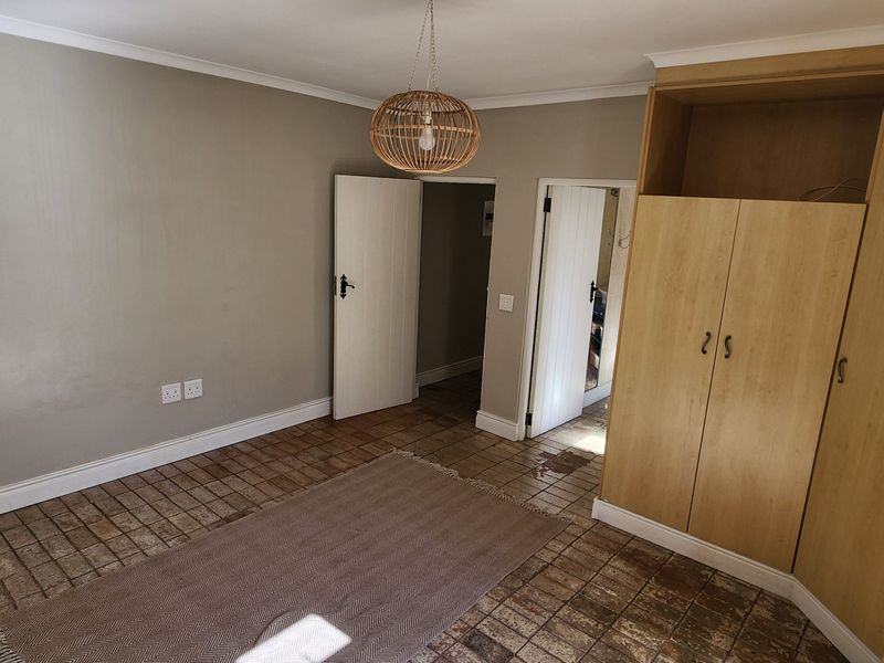 A bedroom featuring built-in wooden cupboards, tiled flooring, and neutral wall tones, offering a blank canvas for personalization.