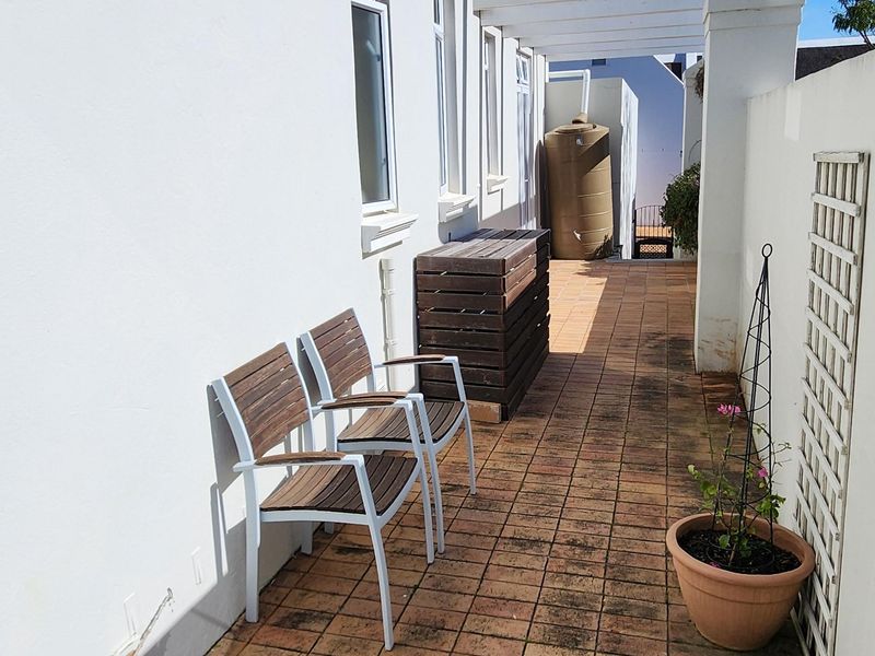 A paved outdoor patio area featuring a pergola structure, boundary wall, and integrated water tank, offering a functional space for outdoor living.