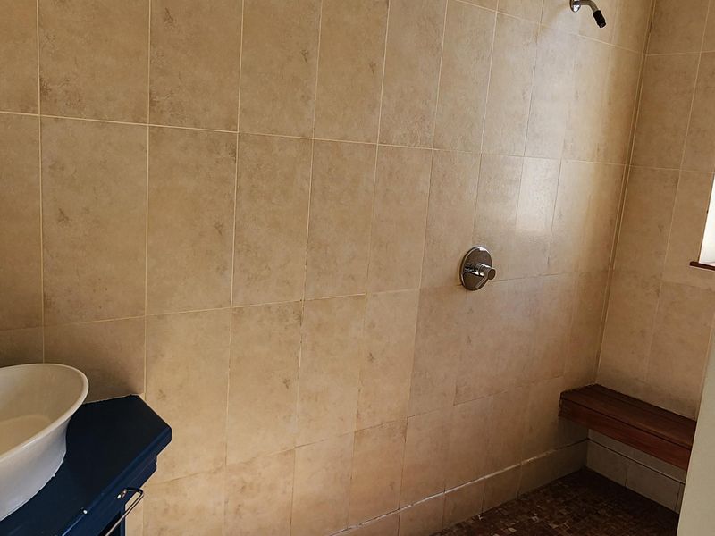 A bathroom featuring a walk-in shower area with tiled walls, a built-in bench, and a vanity sink.
