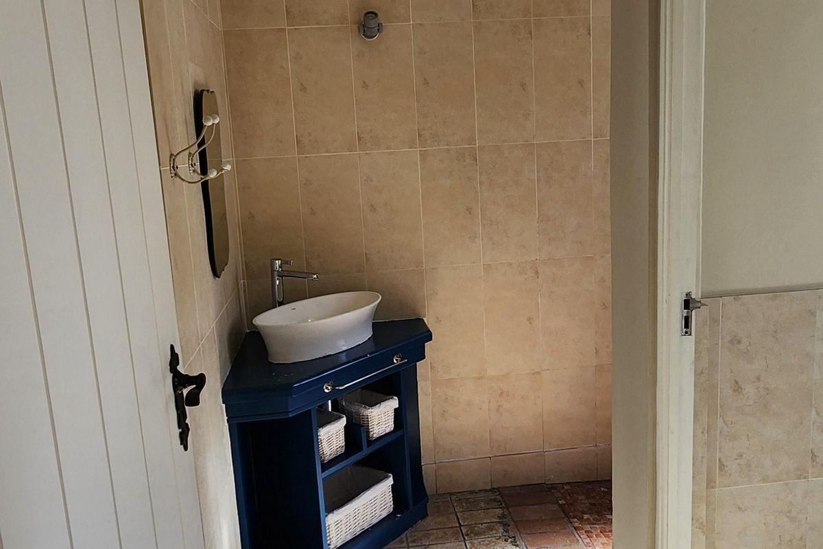 A small bathroom featuring a corner vanity with a vessel sink and terracotta floor tiling.