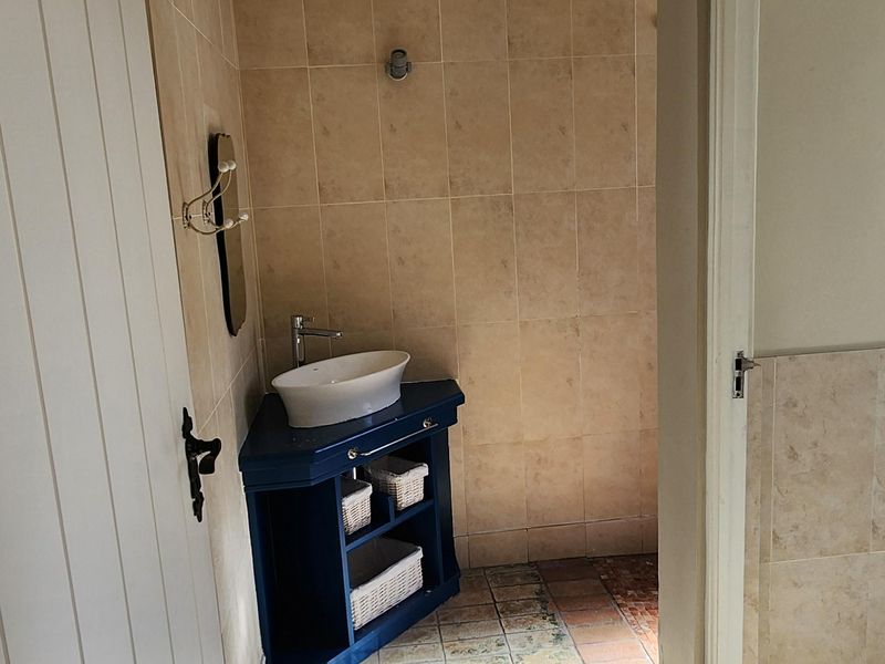 A small bathroom featuring a corner vanity with a vessel sink and terracotta floor tiling.