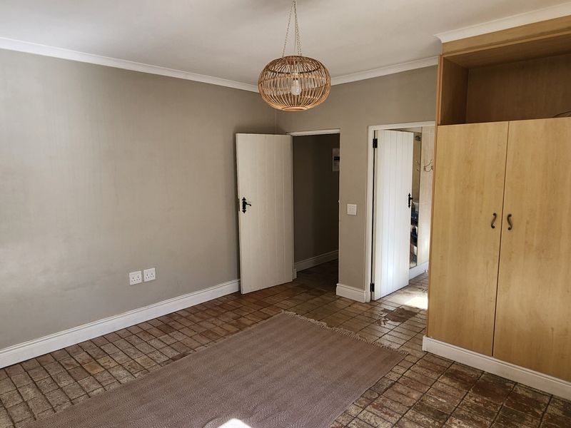 A bedroom featuring built-in wooden cupboards, tiled flooring, and neutral wall tones, offering a functional space ready for personalization.