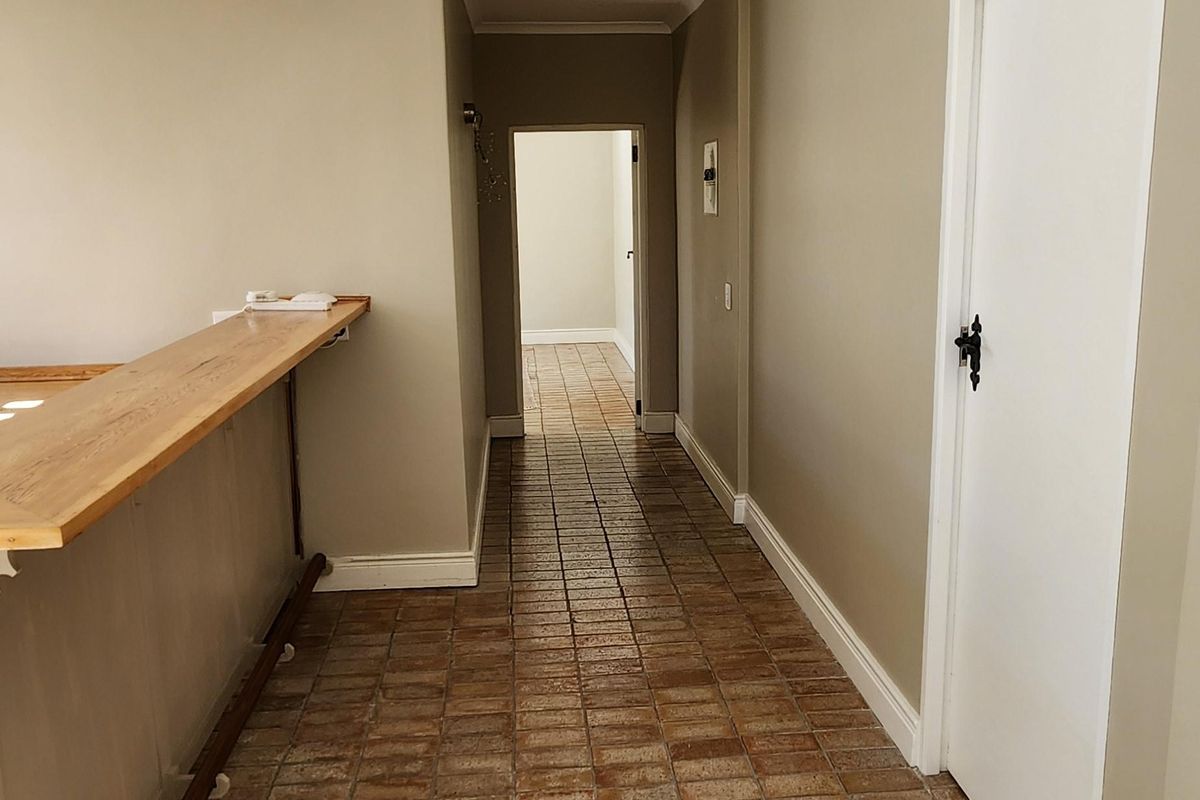 A spacious hallway featuring terracotta tile flooring, a built-in bar counter, and neutral wall tones, leading towards an adjacent room.