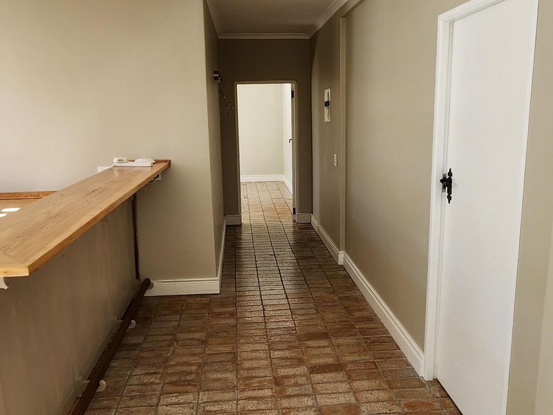 A spacious hallway featuring terracotta tile flooring, a built-in bar counter, and neutral wall tones, leading towards an adjacent room.