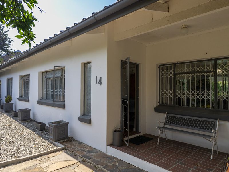 Front elevation of a single-story residence featuring a tiled porch, security gates, and a low-maintenance gravel garden with stone paving.