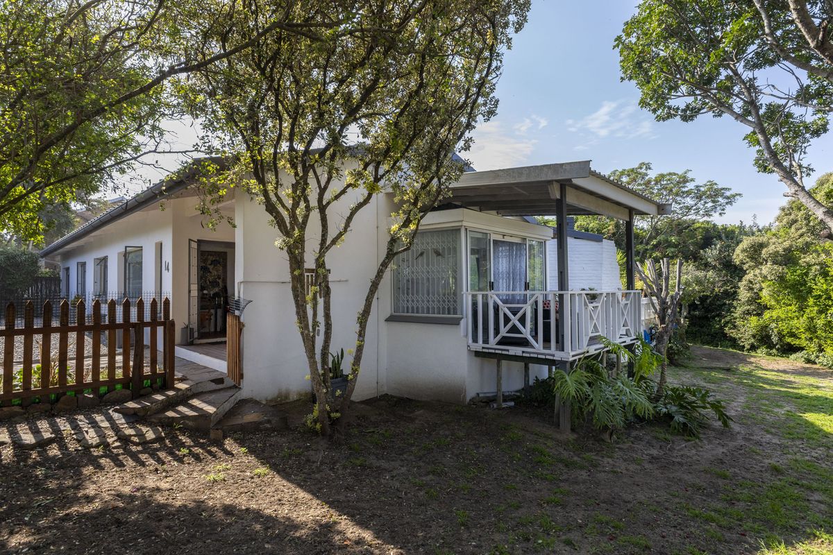Rear view of the house featuring a covered patio with timber balustrade, security gates, and a surrounding garden area.
