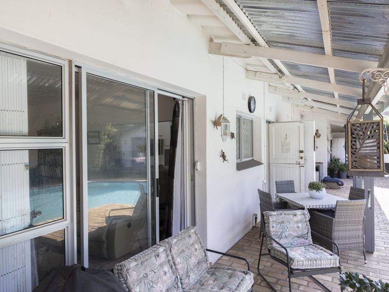 A covered patio area featuring brick paving, sliding glass doors, and a corrugated roof, providing direct access to the pool area.