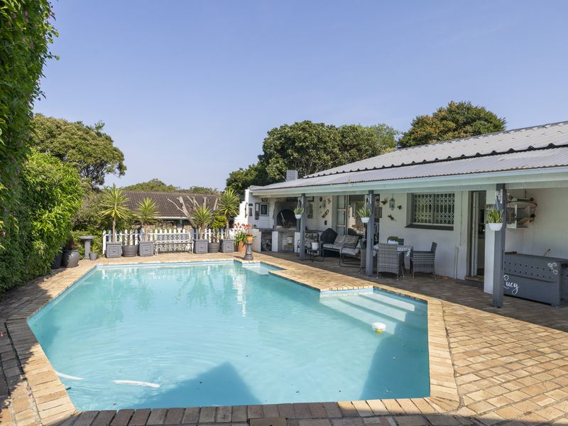 Outdoor pool area featuring a swimming pool, brick paved surround, and a covered patio with a built-in braai.