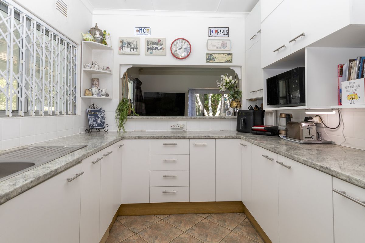 A functional U-shaped kitchen featuring white cabinetry, stone-look laminate countertops, a stainless steel sink, and a convenient serving hatch to the living area.