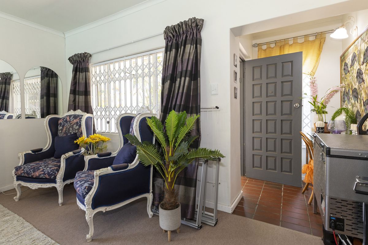 A living room area featuring a panelled entrance door, security gate, and a combination of tiled and carpeted flooring.