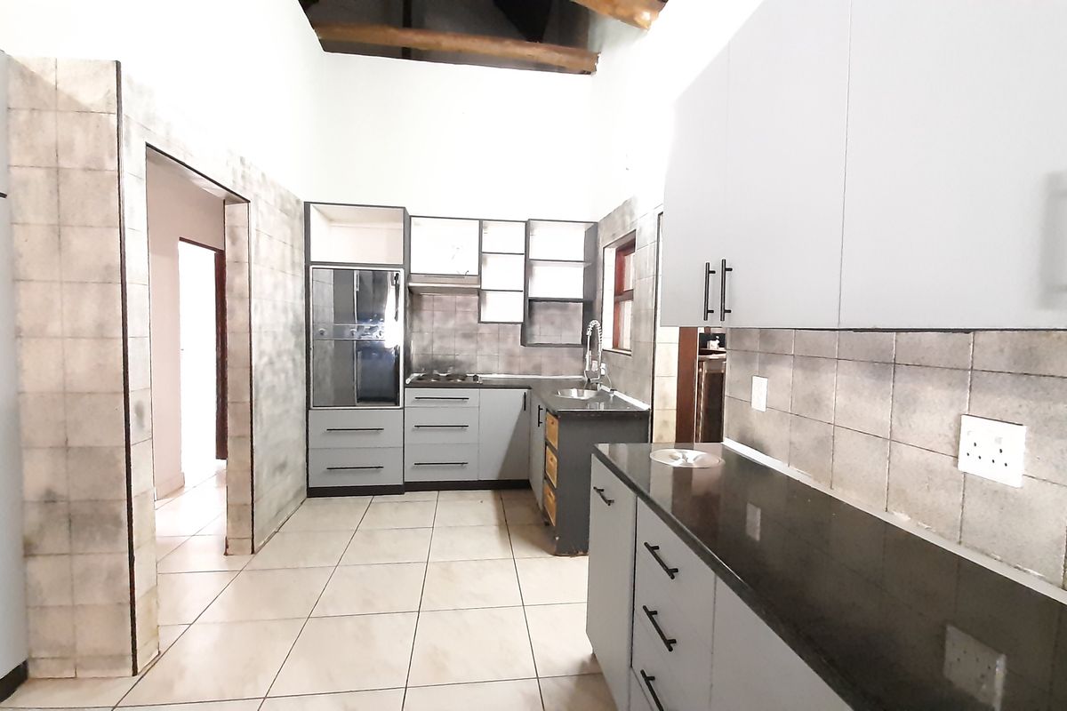 Spacious kitchen featuring built-in cabinetry, stone countertops, integrated oven and hob, tiled backsplash, and exposed timber ceiling beams.