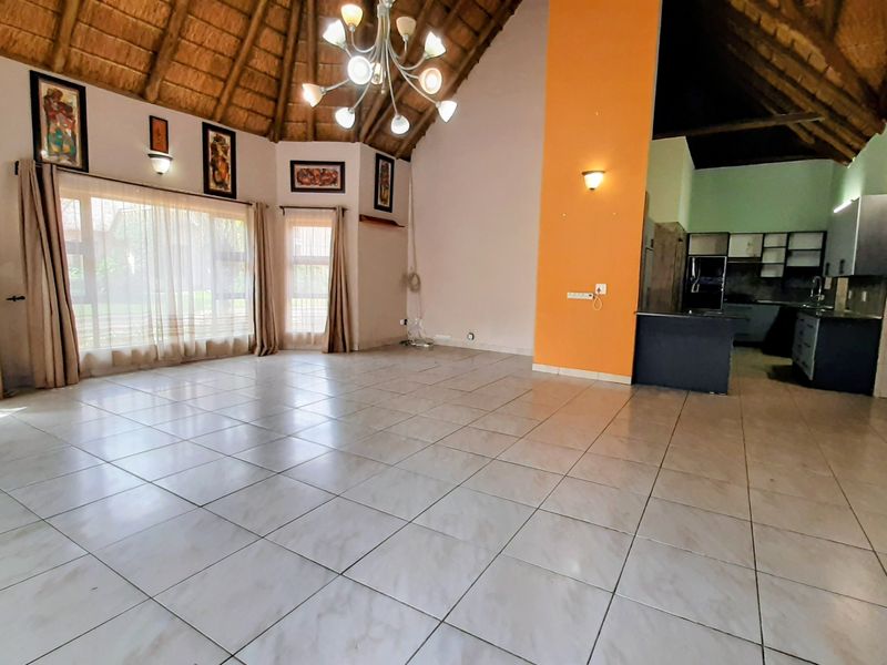 Spacious open-plan living area featuring a high thatched ceiling with exposed rafters, ceramic tiled flooring, and an integrated kitchen with built-in cabinetry.