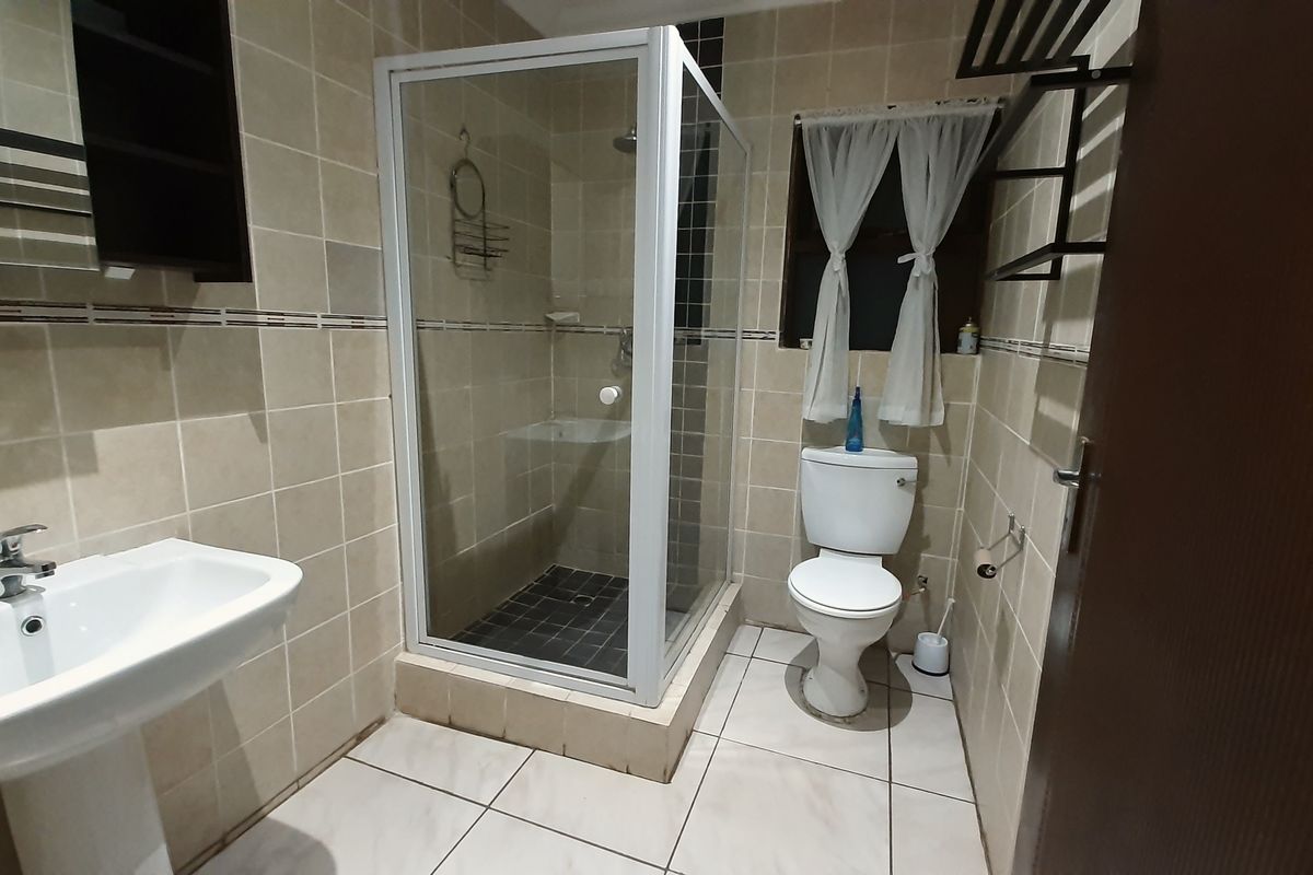 A functional bathroom featuring a pedestal washbasin, a glass-enclosed shower, and a toilet, finished with neutral wall and floor tiles.