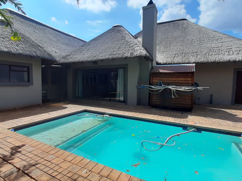 Rear exterior view featuring a swimming pool with brick paving and a traditional thatch roof structure.