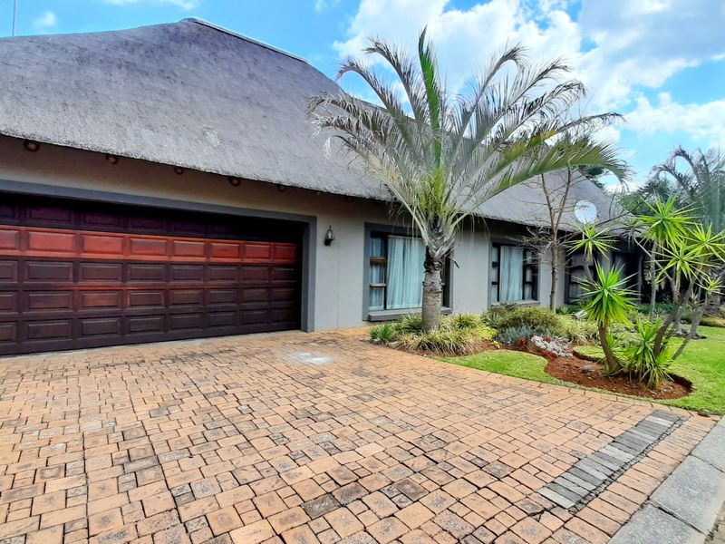 Front elevation of a house featuring a traditional thatch roof, a paved driveway, and a double garage with a well-maintained garden.