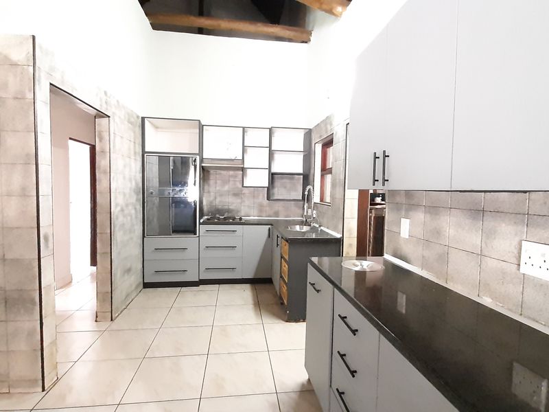 Spacious kitchen featuring built-in cabinetry, stone countertops, integrated oven and hob, tiled backsplash, and exposed timber ceiling beams.