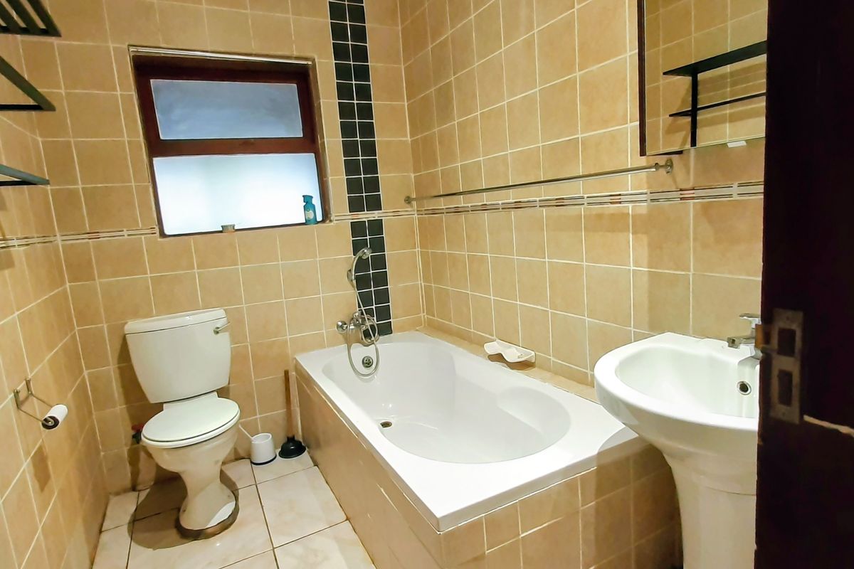 A functional bathroom featuring a bathtub, pedestal basin, and toilet with neutral wall and floor tiling.