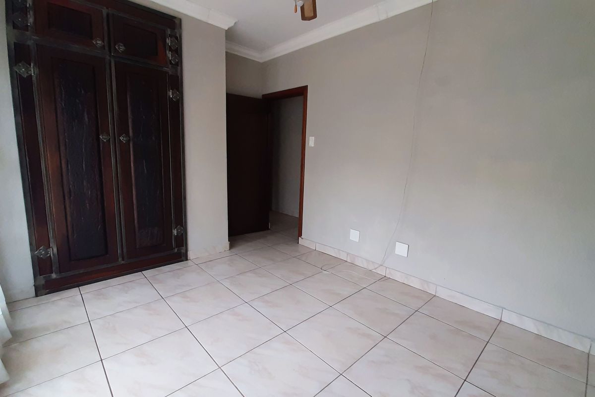 A vacant bedroom featuring ceramic floor tiles, a built-in wooden wardrobe, and coved ceiling cornices.