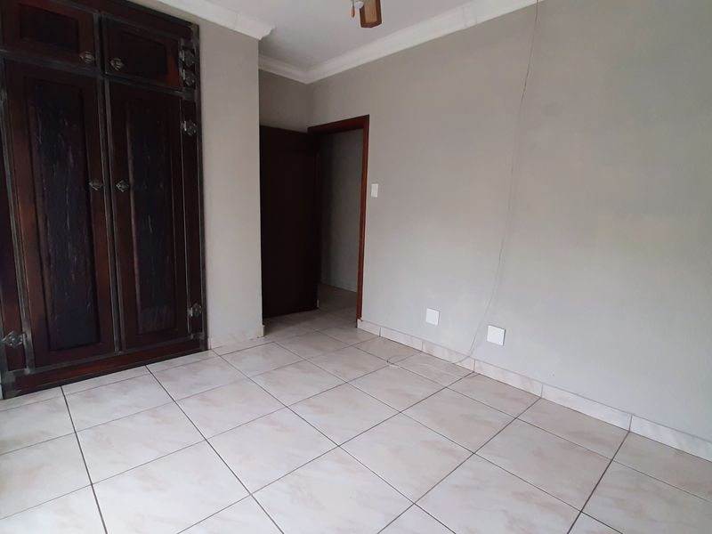A vacant bedroom featuring ceramic floor tiles, a built-in wooden wardrobe, and coved ceiling cornices.