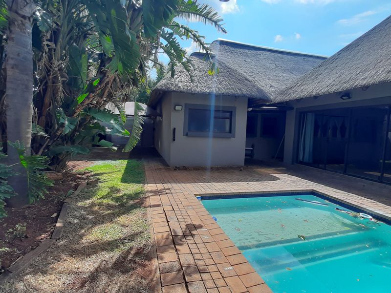 Rear exterior view featuring a swimming pool, brick paved patio area, and a house with a traditional thatched roof.