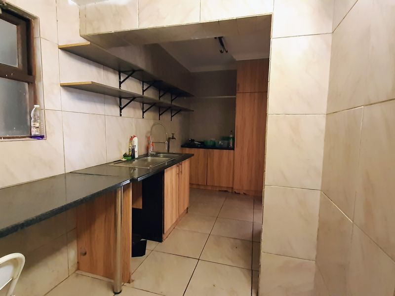 A functional scullery area featuring tiled walls and floors, granite countertops, built-in wooden cabinetry, and open wall-mounted shelving for additional storage.