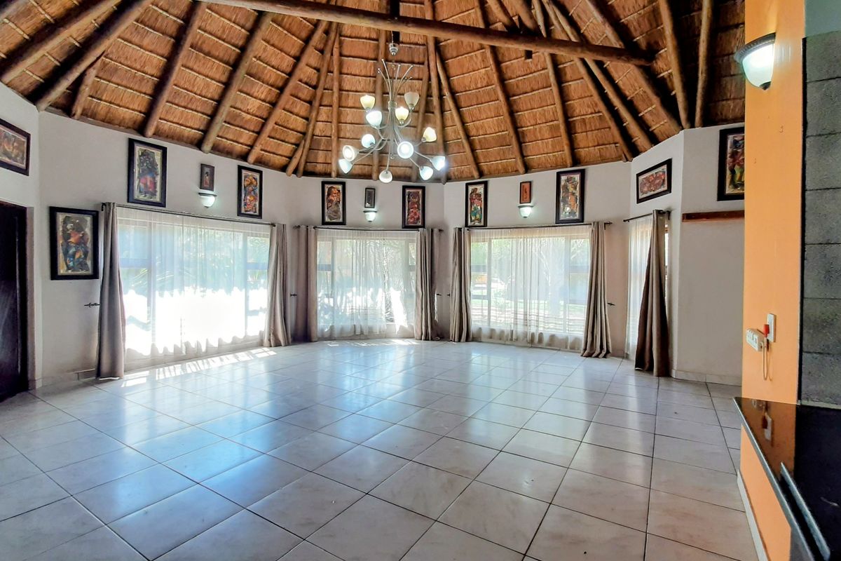 Spacious living area featuring a high vaulted thatched roof with exposed timber rafters, tiled flooring, and large windows providing ample natural light.