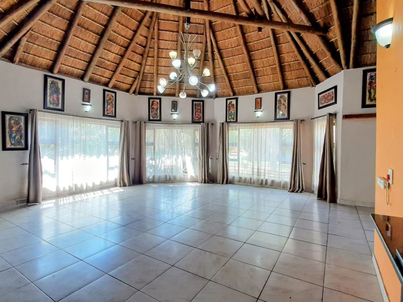 Spacious living area featuring a high vaulted thatched roof with exposed timber rafters, tiled flooring, and large windows providing ample natural light.