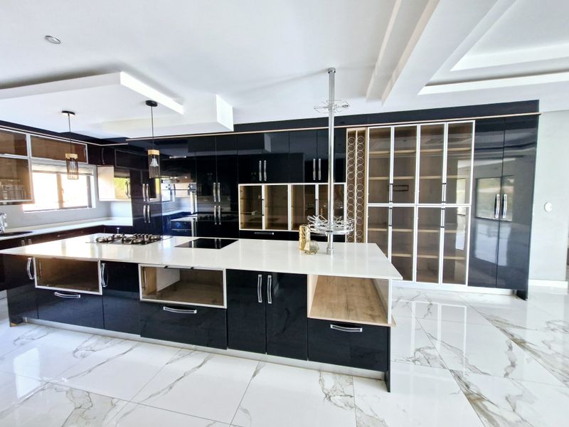 Modern kitchen featuring high-gloss black cabinetry, a large central island with dual cooktops, stone countertops, and elegant marble-look floor tiles.