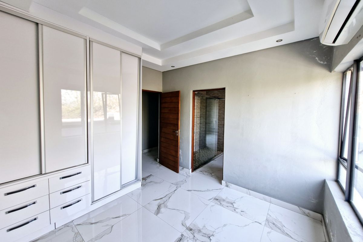Spacious bedroom featuring modern marble-look floor tiles, built-in high-gloss wardrobes, recessed ceiling detail, and an en-suite bathroom.