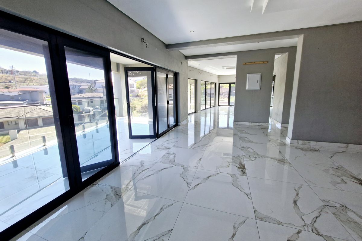 Spacious, modern open-plan living area featuring high-end marble-look floor tiles, recessed ceiling details, and expansive black aluminium stacker doors leading to a balcony.