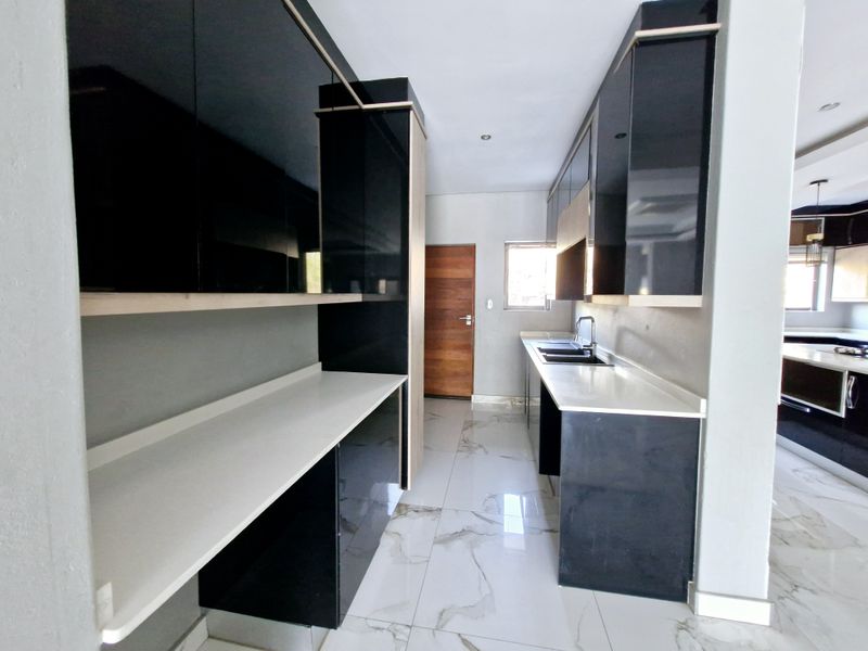 Modern kitchen featuring high-gloss black cabinetry, white stone countertops, double basin sink, and elegant marble-look floor tiles in a clean, contemporary layout.
