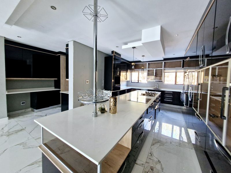 Modern, spacious kitchen featuring a large central island with a gas hob, sleek high-gloss cabinetry, stone countertops, and elegant marble-look floor tiles.