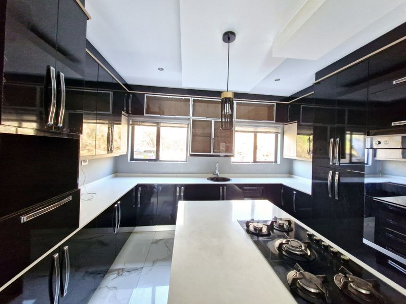 Modern kitchen featuring high-gloss black cabinetry, white stone countertops, a central island with a built-in gas hob, and marble-look floor tiles.