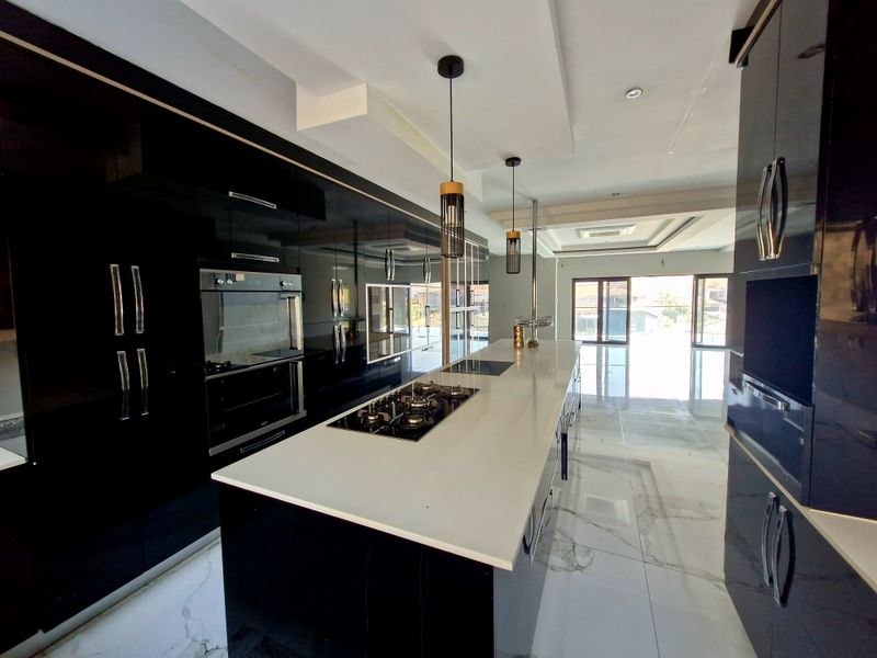 Modern kitchen featuring high-gloss black cabinetry, a large central island with a gas hob, stone countertops, and sleek porcelain floor tiles.
