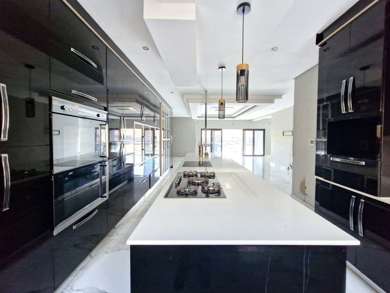 Modern kitchen featuring high-gloss black cabinetry, a large central island with a gas hob, built-in oven, and sleek stone countertops.